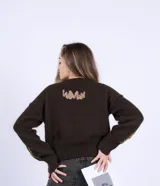 Sweater de lana merino color chocolate, tejido a dos agujas con diseño de flores bordadas en color amarillo en el pecho y parche decorativo con texto en la parte inferior.