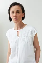 Remera blanca de algodón con mangas cortas y cuello redondo con abertura tipo gota. Presenta un delicado bordado floral en la parte superior delantera.