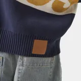 Cardigan de punto grueso color azul marino con cierre frontal de cremallera metálica, cuello tipo polo y corte cuadrado. Presenta un diseño de bloques de color con una franja blanca horizontal en el cuerpo y las mangas, y el logotipo gráfico 'EME' en tono mostaza en el pecho.