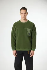 Buzo de hombre color verde oliva, confeccionado en tejido polar texturizado (tipo borrego o sherpa). Presenta un canesú horizontal en el pecho y un bolsillo utilitario con cierre en el lado izquierdo del pecho, de material liso contrastante. Tiene cuello redondo y puños y cintura de punto acanalado.