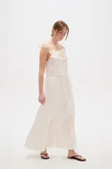 Vestido largo de algodón color blanco, con tirantes finos ajustables con lazos en los hombros, escote recto decorado con apliques florales tridimensionales, cordón ajustable en la cintura y falda larga con volados horizontales.
