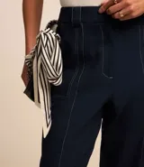 Pantalón de vestir negro, estilo carrot (holgado en cadera y ajustado en tobillo), de cintura alta con trabillas y cierre tradicional. Presenta recortes verticales con costura aparente en el frente.