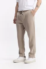 Pantalón de jogging color beige, confeccionado en algodón y poliéster, con cintura elástica y cordón ajustable. Diseño clásico sin puño en los tobillos.