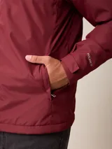 Campera de nylon gris con capucha, cierre frontal completo y bolsillos laterales. Presenta un diseño minimalista con logo bordado en el pecho.