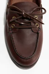 Zapatos náuticos de cuero color marrón con cordones frontales, ojales metálicos dorados y costura de mocasín en la puntera.