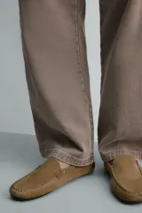 Mocasín de vestir para hombre confeccionado en piel con acabado de serraje en color mostaza. Presenta un diseño de horma redonda con detalle de tachas metálicas en los laterales y suela de goma flexible.