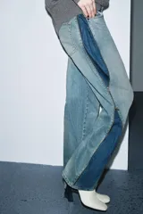 Jeans de tiro medio, corte recto y ancho, en denim azul claro con efecto lavado y desgaste. Presenta cierres metálicos completos a lo largo de las costuras laterales exteriores de ambas piernas.
