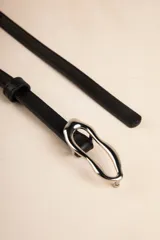 Cinturón fino negro de símil cuero con hebilla metálica irregular plateada.