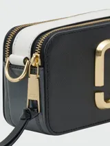 Cartera crossbody Marc Jacobs modelo The Snapshot, color tostado con herrajes dorados y logo frontal metálico. Incluye correa ajustable y extraíble con diseño de marca estampado.