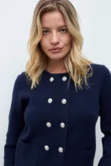 Chaqueta tejida de punto en color azul marino, con diseño de doble botonadura frontal y bolsillos aplicados. Presenta un cuello desmontable en tono claro y mangas largas.