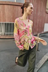Blusa de manga larga con estampado floral en tonos rosados, verdes y beige. Presenta escote en pico con detalle de abalorios colgantes y cierre frontal con botones.
