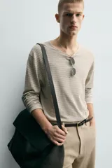 Jersey de punto de corte relajado, con cuello redondo amplio y mangas largas. Presenta un diseño de rayas horizontales finas en contraste sobre fondo beige.