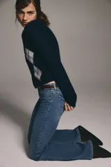 Jeans de denim azul medio con ligero efecto desgastado, tiro bajo y corte acampanado (bootcut) desde la rodilla. Presenta cierre y botón frontal, bolsillos delanteros decorativos y bolsillos abiertos traseros.