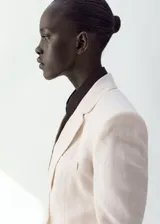 Blazer de lino color beige, de diseño recto con cuello en V, solapas con muesca, mangas largas, bolsillos de ribete delanteros y cierre frontal de un botón.