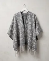 Poncho de dama color gris con diseño geométrico de líneas blancas entrelazadas y terminación de flecos en el ruedo.