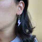 Aros de acero quirúrgico plateado con dije de rayo color lila.