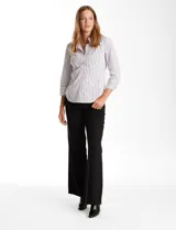 Camisa entallada de algodón con estampado de rayas verticales en tonos blanco y gris. Presenta cuello con solapa, escote en V, cierre frontal con botones y mangas tres cuartos con puños anchos. El diseño incluye paneles laterales elastizados para un ajuste flexible y ruedo redondeado.