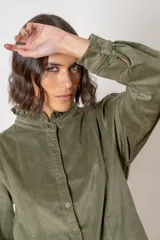 Camisa de pana color verde oliva, con cuello alto con volados, cierre frontal de botones y mangas largas con puños.