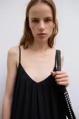 Vestido midi de color negro, confeccionado en tejido fluido, con escote en V y tirantes finos ajustables. Presenta frunces en el pecho y un volante en el bajo.
