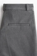 Pantalón sastrero de tiro alto con corte acampanado y pliegues frontales. Cuenta con cierre de botón y bolsillos decorativos.
