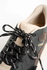 Zapatilla urbana de cuero con diseño de paneles en tonos negro, marrón oscuro y beige. Presenta una suela de plataforma robusta en color beige y cordones jaspeados.