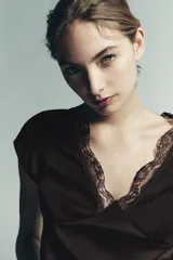 Top color marrón oscuro, con escote en V y mangas cortas. Presenta detalles de pliegues verticales en el delantero y terminaciones con encaje a tono en el escote y el ruedo inferior.