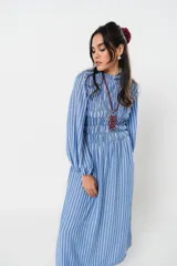 Vestido largo a rayas verticales azules y blancas, con manga globo y diseño de nido de abeja con hilo elástico hasta la cintura. Cuello alto fruncido y falda amplia con caída fluida.