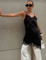 Vestido negro de satén con encaje en escote y ruedo, de corte asimétrico y breteles finos.