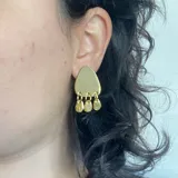 Par de aros colgantes plateados con forma triangular y tres dijes redondos colgando de la base.