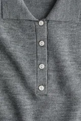 Buzo de punto suave color gris, con cuello clásico estilo polo, tapeta con botones frontales, mangas largas y hombreras.
