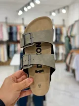 Sandalias de dos tiras negras con hebillas metálicas ajustables, plantilla anatómica y suela plana.