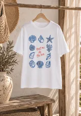 Remerón blanco de manga corta, con cuello redondo y estampado central de temática marina con caracoles, estrellas de mar y la frase "Meet me by the sea".