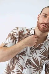 Camisa de manga corta con estampado botánico de hojas en tonos azul y blanco. Presenta cuello clásico, cierre frontal abotonado y corte slim.