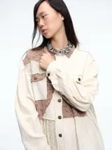 Vestido camisero de corte midi con diseño patchwork que combina paneles en tonos crudo y marrón con estampados florales sutiles. Presenta cierre frontal con botones, cuello camisero y mangas largas con puños.