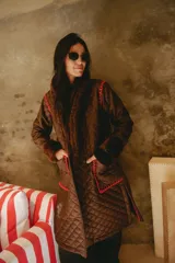 Campera larga acolchada color marrón, con diseño matelassé, detalles de piel sintética en el cuello y puños, y bordados artesanales en crochet color rojo en los bolsillos y costuras.