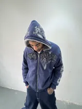 Campera reversible con cierre frontal. Un lado confeccionado en algodón azul marino con estampa plastisol, bordados con apliques y capucha. El otro lado presenta un diseño de polar de pelo largo en color gris. Posee corte oversize, puños y ruedo acanalados.