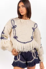 Sweater de punto 100% lana merino en color marfil, de calce holgado y cuello redondo, con detalles bordados en azul marino y flecos decorativos en el bajo y las mangas.