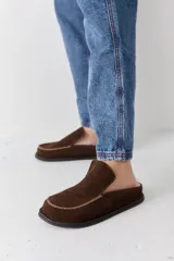 Zueco tipo mocasín de gamuza color marrón, con costuras decorativas en contraste en la puntera y suela plana.