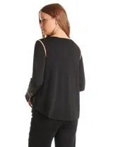 Blusa negra de crepe elastizado con ribetes en contraste color beige que recorren el escote en V, la línea central del frente y las costuras de los hombros. Tiene mangas largas con puños abiertos, abertura lateral y botón metálico.