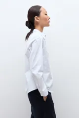 Camisa blanca de manga larga con cuello clásico y botones frontales ocultos.