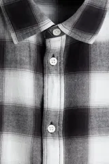 Camisa de franela de algodón suave con estampado a cuadros, cuello inglés, cierre frontal de botones, mangas largas con puños abotonados y bajo redondeado.