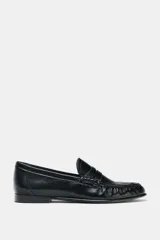 Mocasín plano de cuero negro con detalle de antifaz, copete subido y acabado fruncido en la parte delantera.
