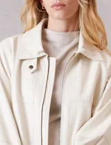 Campera bomber de eco cuero color beige, con cuello camisero, cierre frontal metálico y bolsillos delanteros con solapa y botón a presión. Presenta mangas largas con puños abotonados y ruedo trasero elastizado.