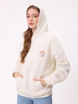 Canguro color crema con capucha y estampado grande en la espalda de un sol con un ojo, montañas, mariposas y texto.