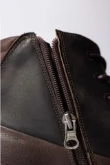 Championes de caña alta confeccionados en cuero marrón oscuro, con cordones al tono y suela de goma color caramelo.