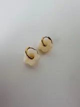 Aros de acero quirúrgico dorados con argolla pequeña y dije en forma de flor color blanco marfil.