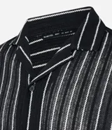 Camisa masculina modelo boxy, confeccionada en punto, con cuello polo, manga corta, cierre por botones y estampa de rayas verticales blancas sobre fondo negro.