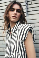 Vestido midi de diseño combinado con cuerpo de camisa sin mangas a rayas verticales en blanco y negro, y falda negra de corte recto. Presenta cuello solapa, cierre frontal con botones y cinturón negro con hebilla metálica dorada.