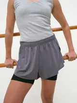 Short deportivo de color gris, confeccionado con tela dry fit, con cintura elastizada y aberturas laterales. Cuenta con calza interna negra ajustada.