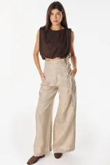 Pantalón de lino blanco de corte ancho y fluido, con cintura alta que incorpora una sobrepretina ancha desmontable con pliegues horizontales.